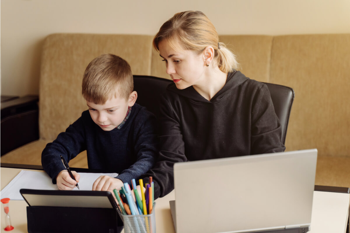 Woman helps child with homework at desk.