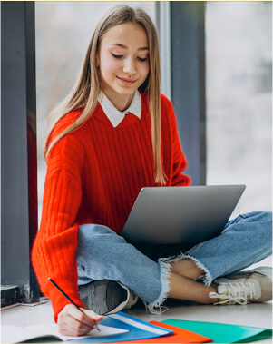 Woman drawing on paper with laptop nearby.