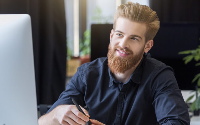 Man with beard working at computer desk.