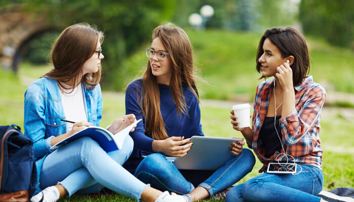 Three women studying outdoors on grass.