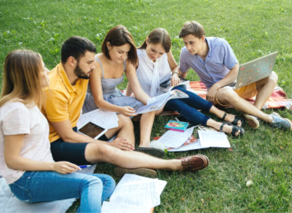 Group of students studying on grass with laptops