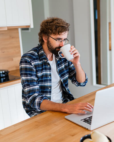Man drinking coffee while using laptop at home.